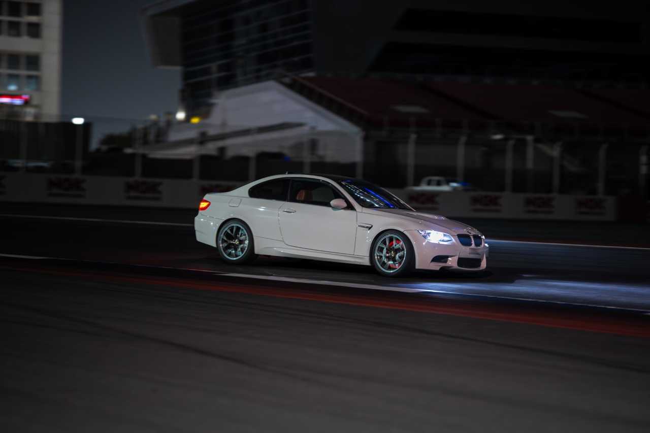 A white, modified BMW M3 E92 coupe on a night track | ATOMIC-SHOP
